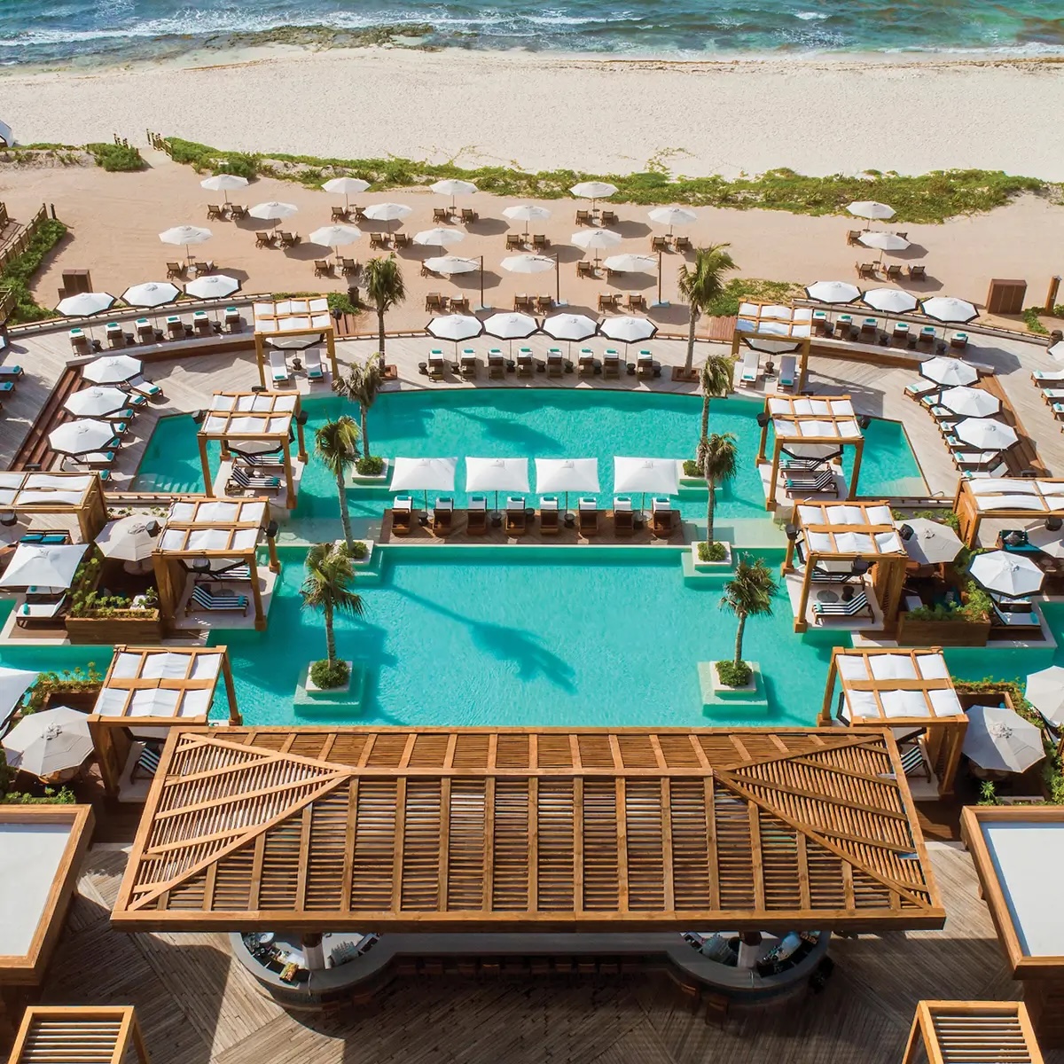 Aerial view of the infinity pool at Vidanta Riviera Maya next to the beach, featuring loungers, palapas, and cabanas