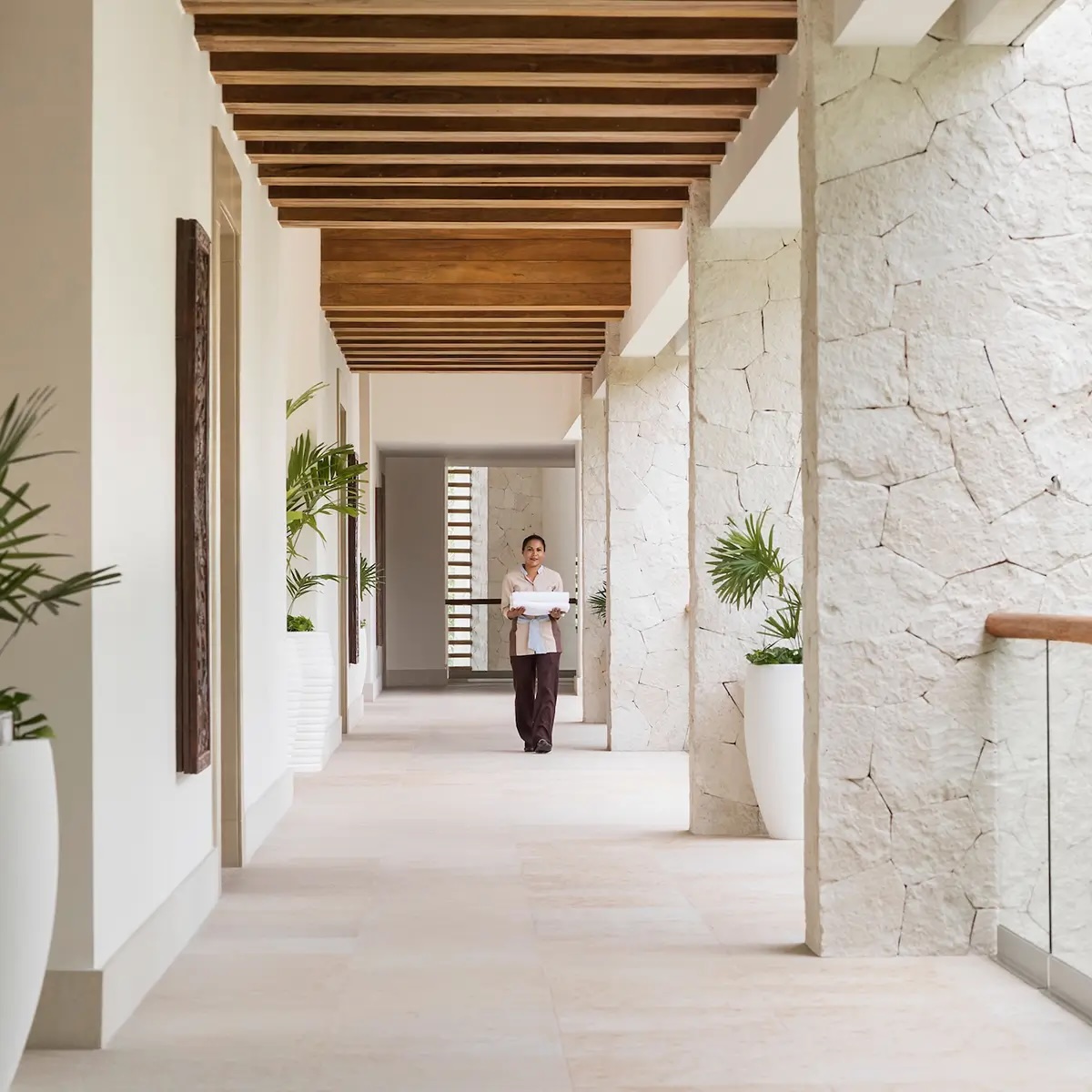Stone and wood corridor at Vidanta Riviera Maya, with housekeeping staff providing service